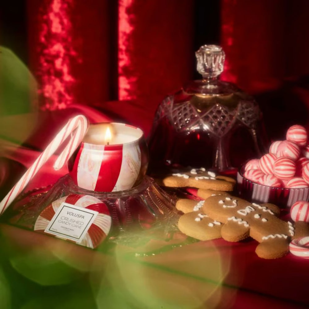 Decorative Christmas scene with cookies, candy, and a lit candle on a reflective surface.