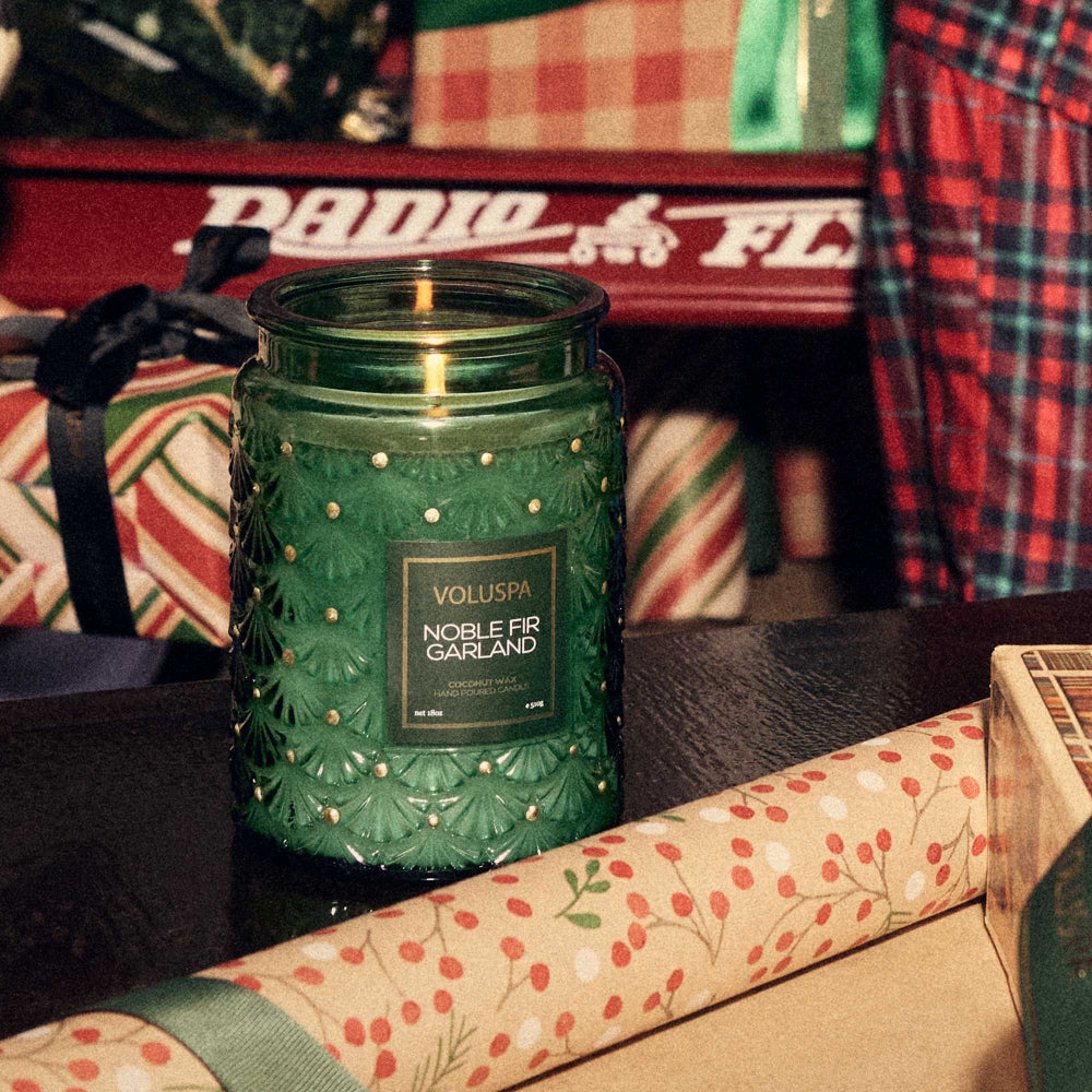 Green Voluspa candle with decorative packaging on a table.