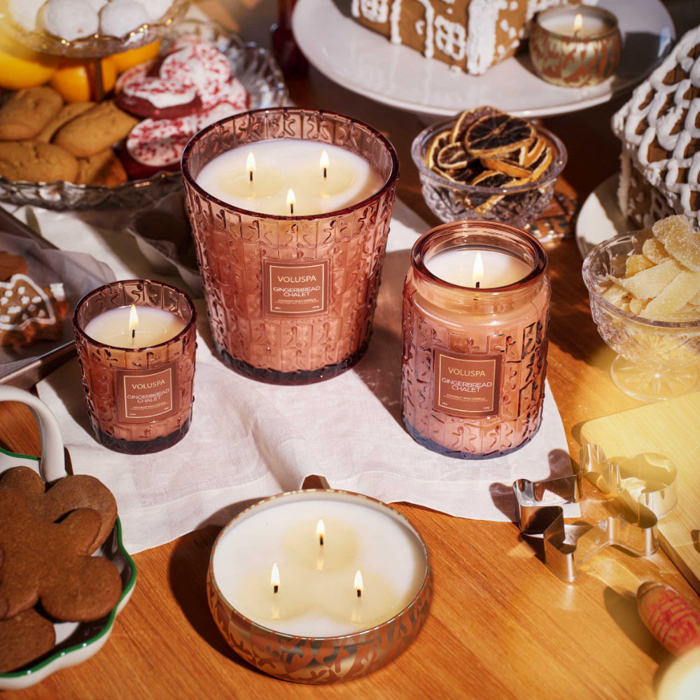 Votive candles with Voluspa branding on a festive table with gingerbread cookies and decorations.