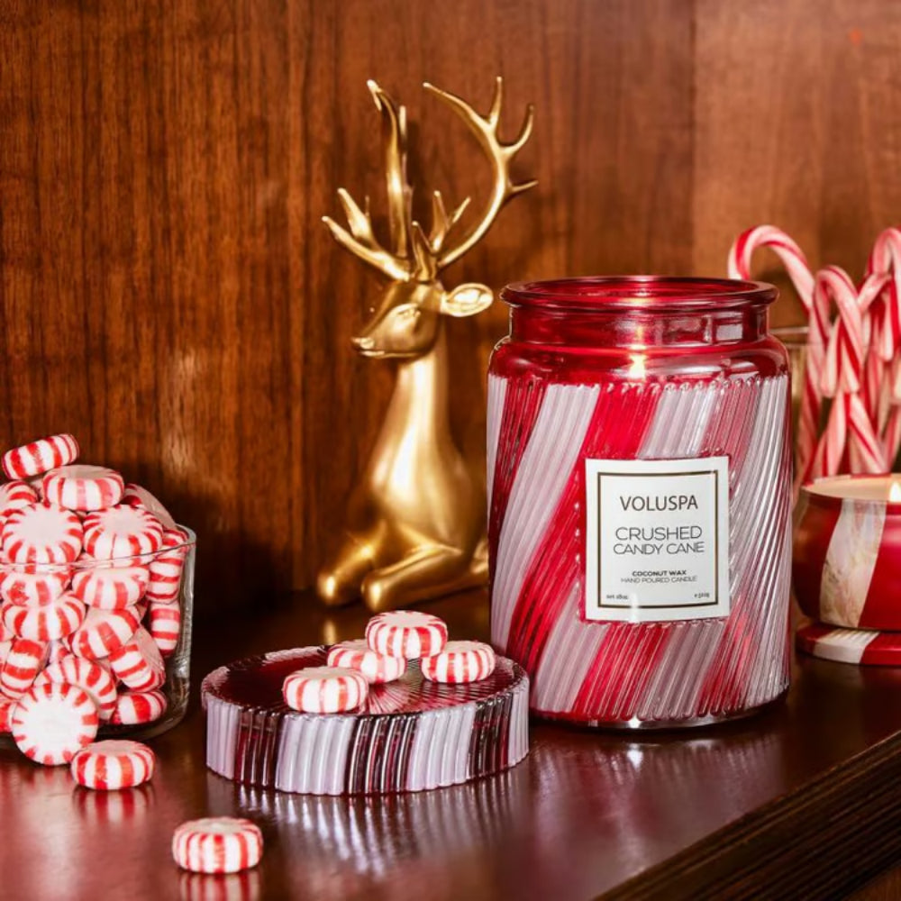 Decorative setup with Voluspa candle, candy canes, and a gold deer statue on a wooden surface.