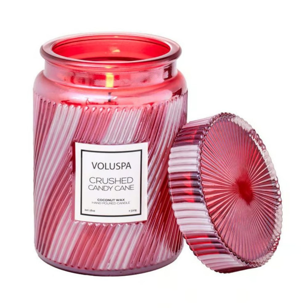 A red striped glass jar candle with its matching lid leaning against it on a white background. The label reads 'VOLUSPA CRUSHED CANDY CANE'.