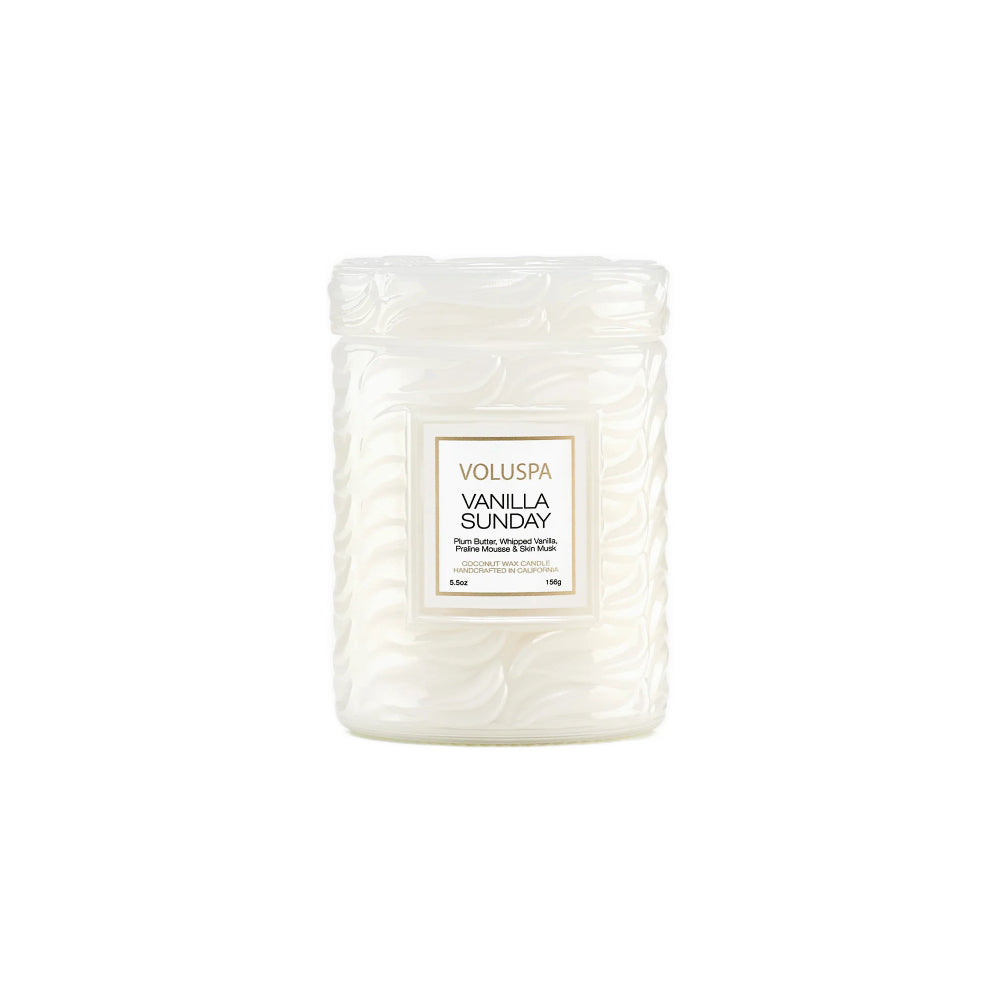 A Voluspa Vanilla Sunday scented candle in a textured, ribbed glass jar with a white wax fill and a white label with gold borders, set against a plain white background.