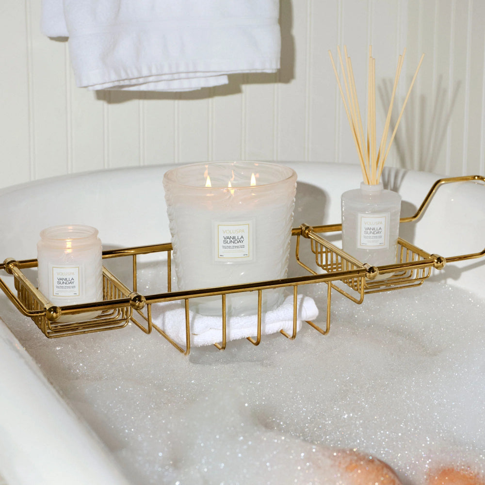 Candles in a bathtub with a gold tray and white towels.