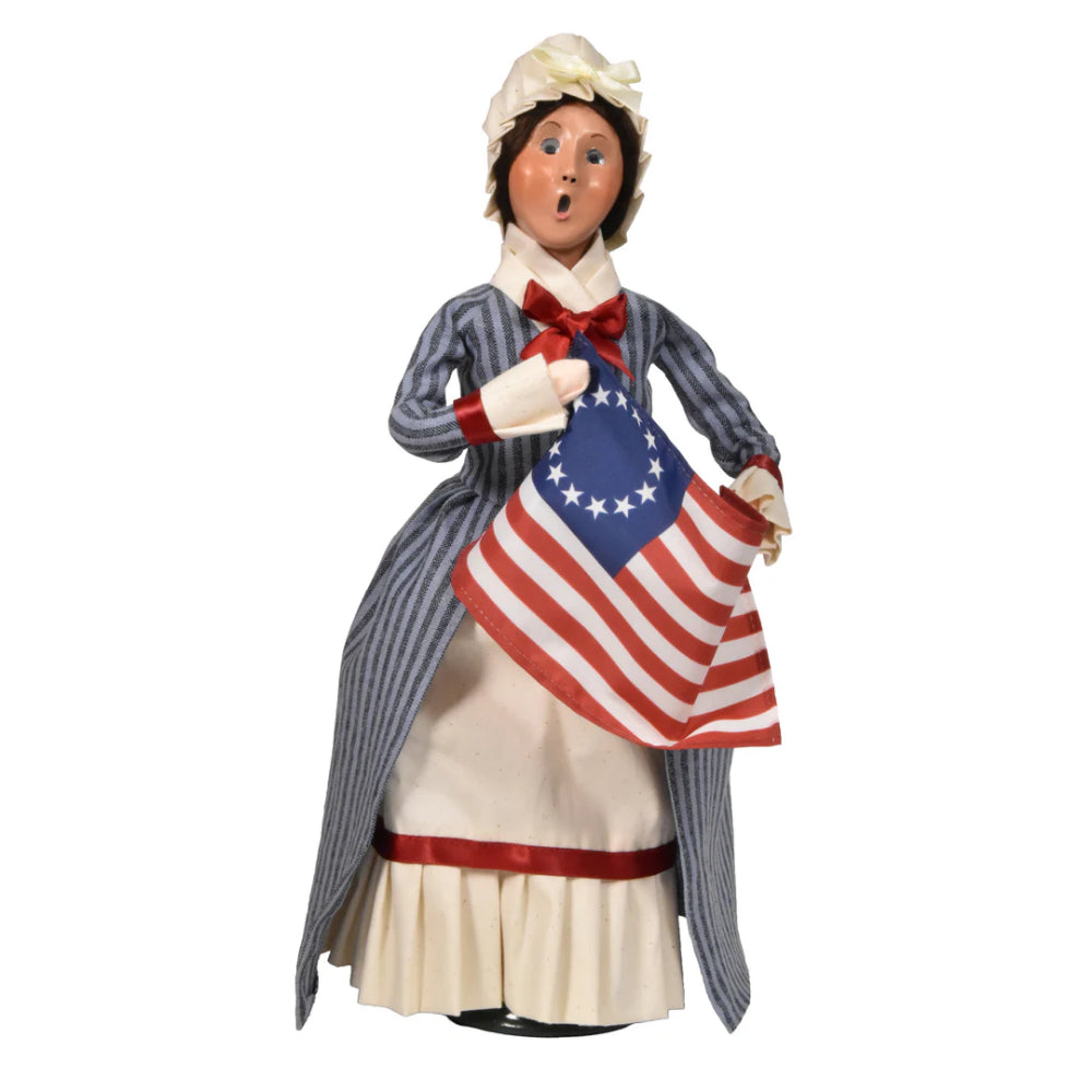 Figurine of a caroling Betsy Ross in historical attire holding an American flag on a white background