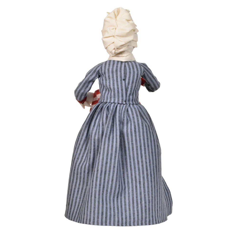 Back side photo of a figurine of a  caroling Betsy Ross in historical attire holding an American flag on a white background