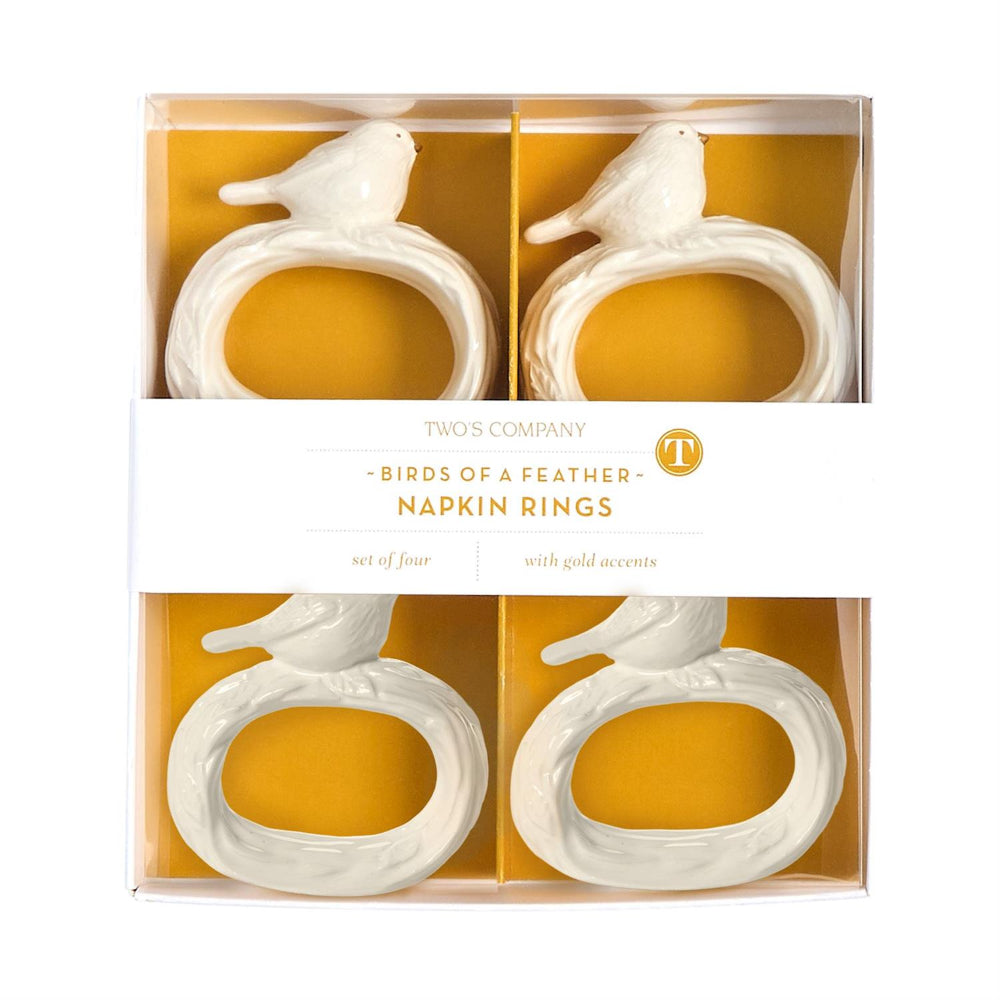 Packaged set of white bird-shaped napkin rings with gold accents on a yellow background in set package. 