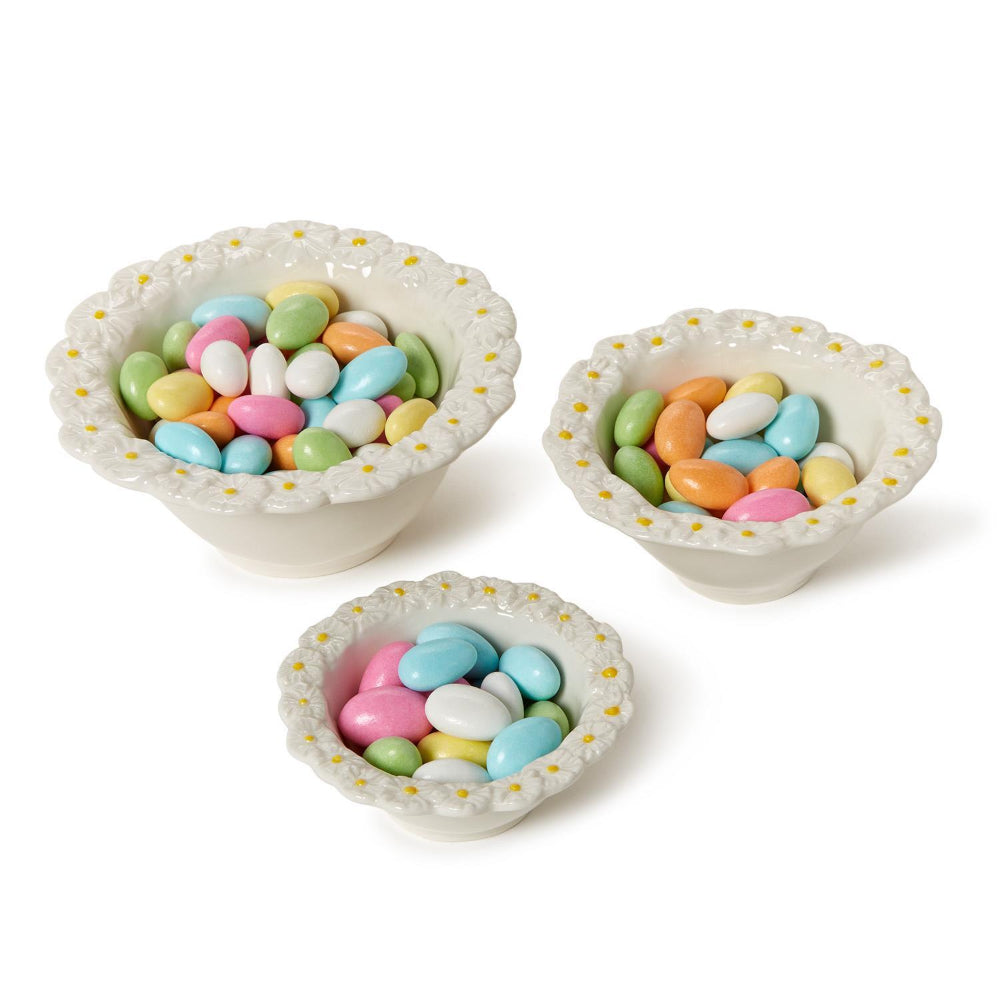 Three small ceramic bowls with a daisy floral pattern on the rim  filled with colorful candies on a white background