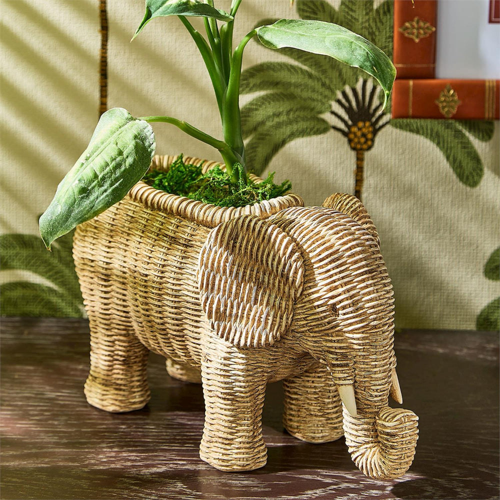 Woven elephant planter with a plant on a wooden surface.