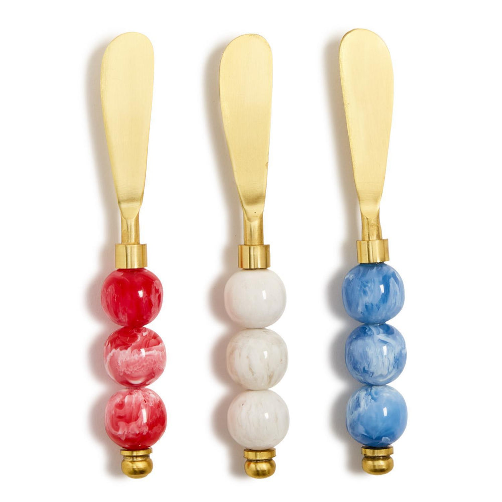 Three gold cheese knives with colorful red, white and blue resin  marble handles in a  on a white background