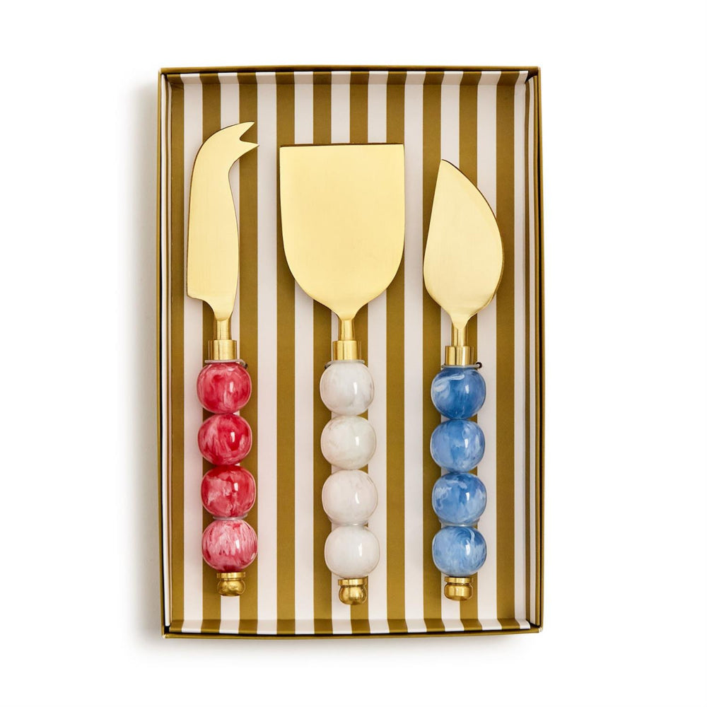 Set of three gold-handled cheese knives with colorful red,white and blue marble handles in a gold and white striped box on a white backround 