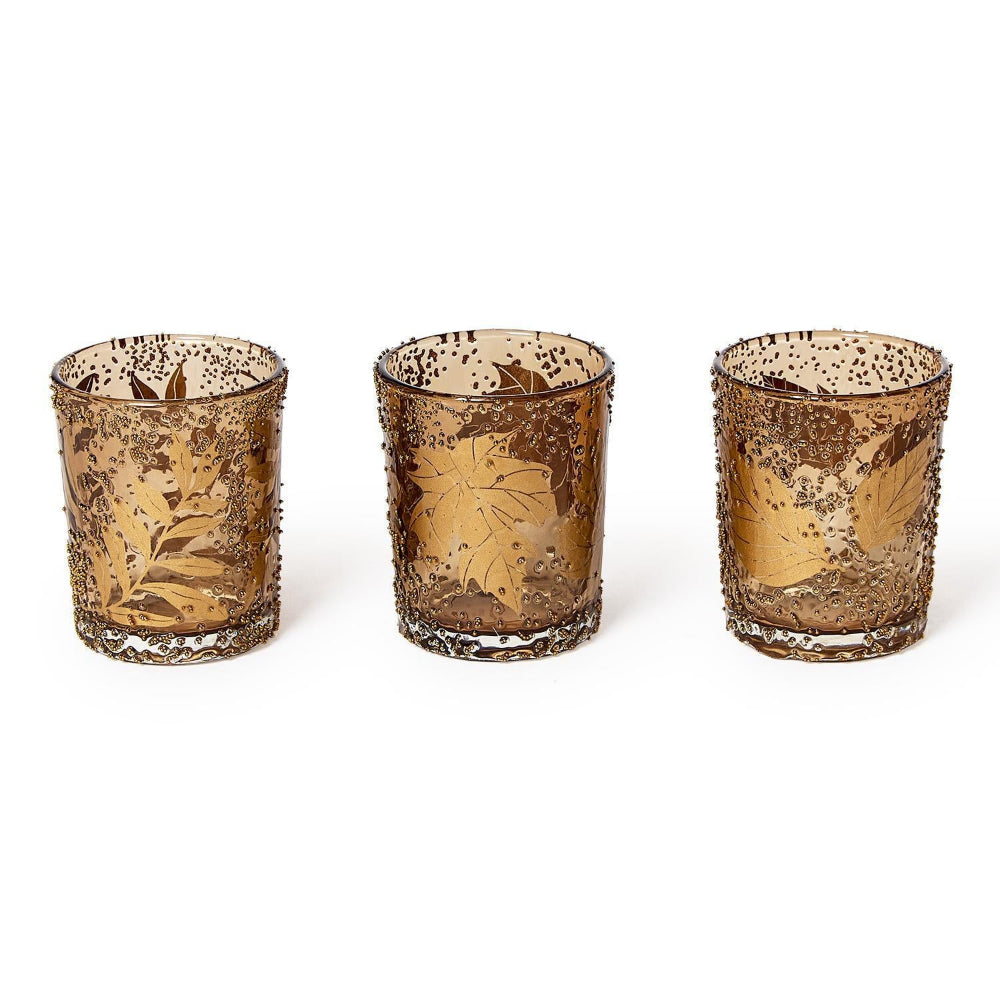 Three decorative glass candle holders with leaf patterns on a white background.
