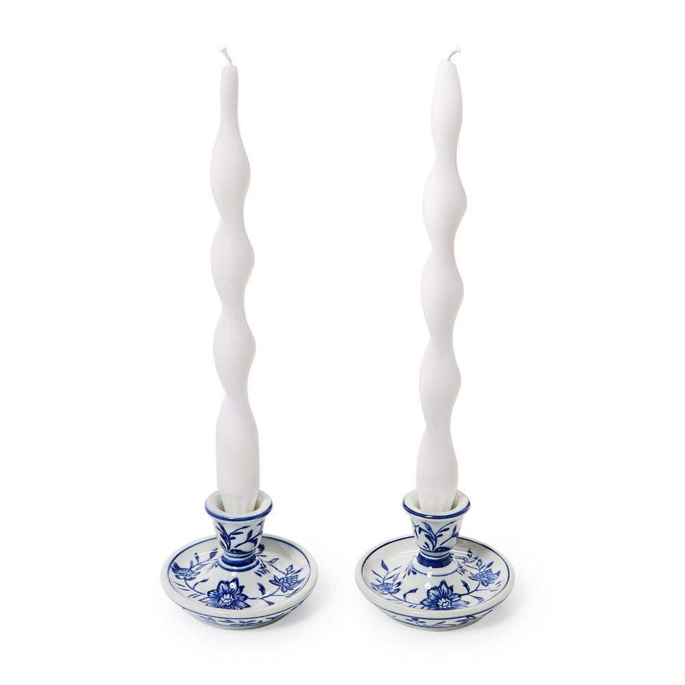 A pair of tall white spiral taper candles in blue and white floral ceramic candlesticks on a white background.