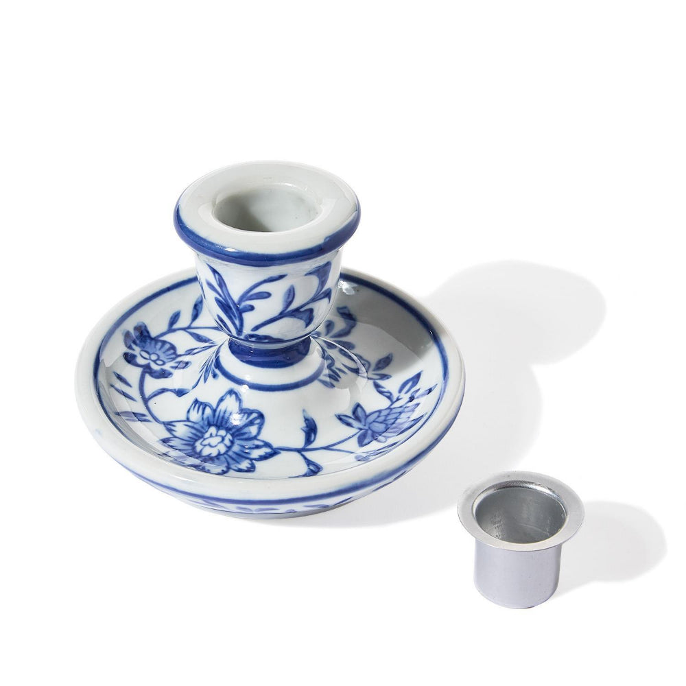 A blue and white floral porcelain candlestick holder with a matching base and a separate small metal cup, photographed on a white background with soft shadows.