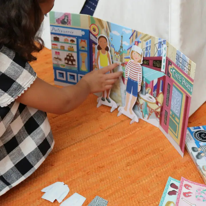 Child playing with a colorful paper doll set on an orange surface