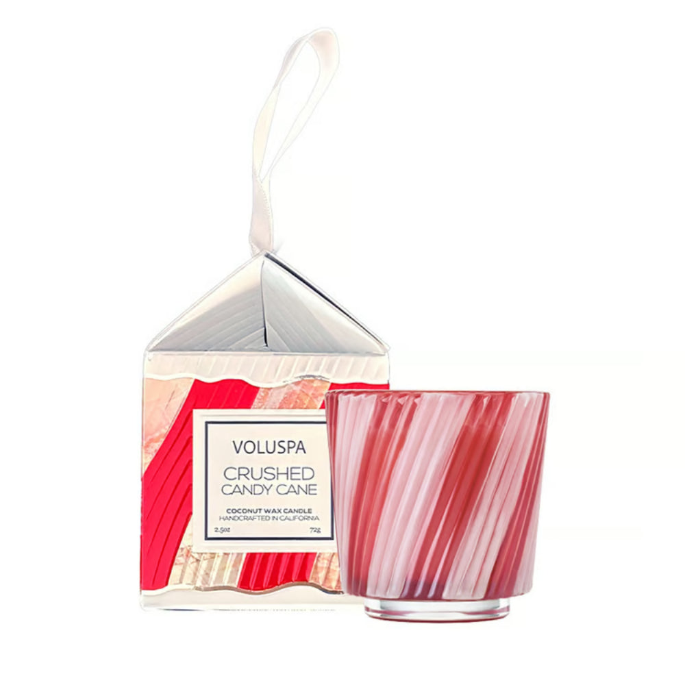Voluspa Crushed Candy Cane hand-blown glass candle in a pink striped glass jar, shown next to its white and red patterned packaging box with a hanging loop on a white background.