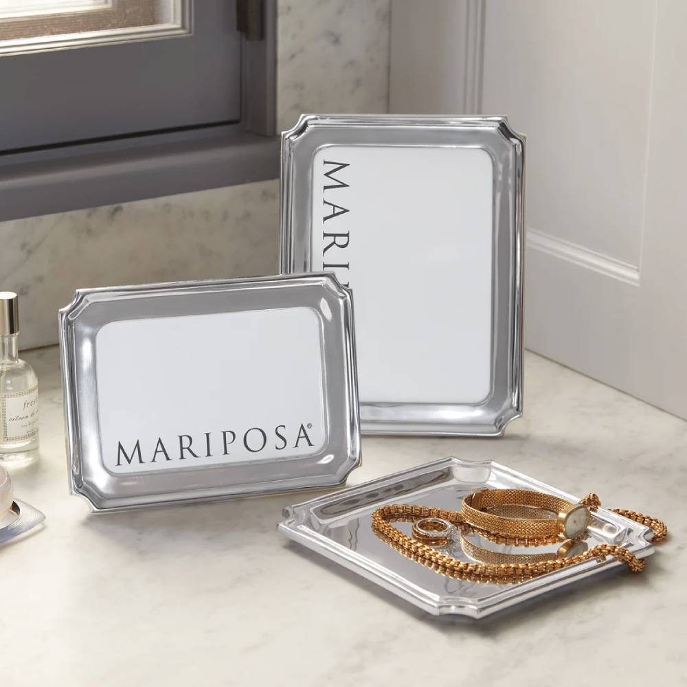 Two silver metal picture frames with white inserts and the brand name 'MARIPOSA' printed in black, arranged on a light marble surface next to a window.