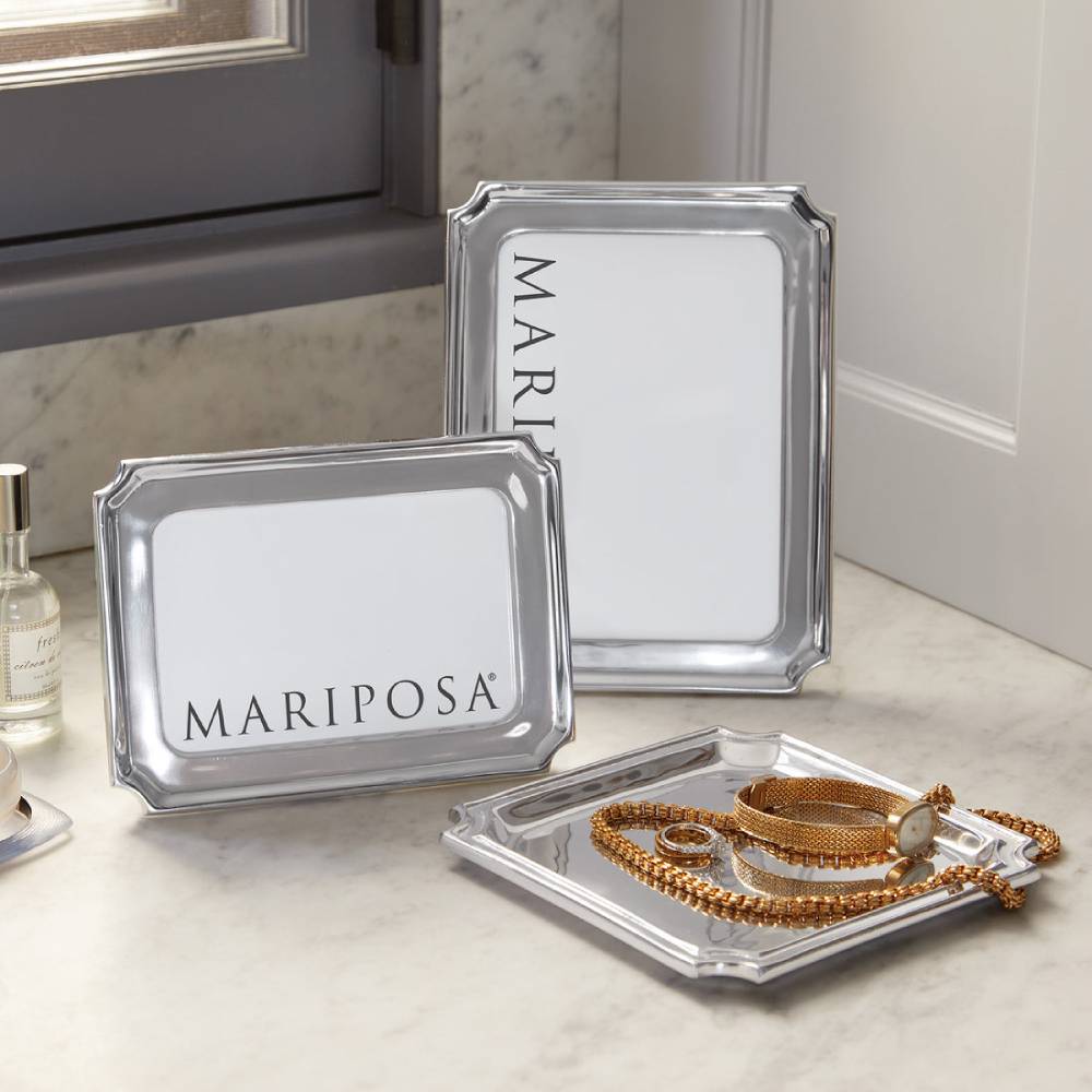 Two silver metal picture frames with white inserts, with the text 'MARIPOSA' visible in the display, arranged on a light marble countertop next to a window.