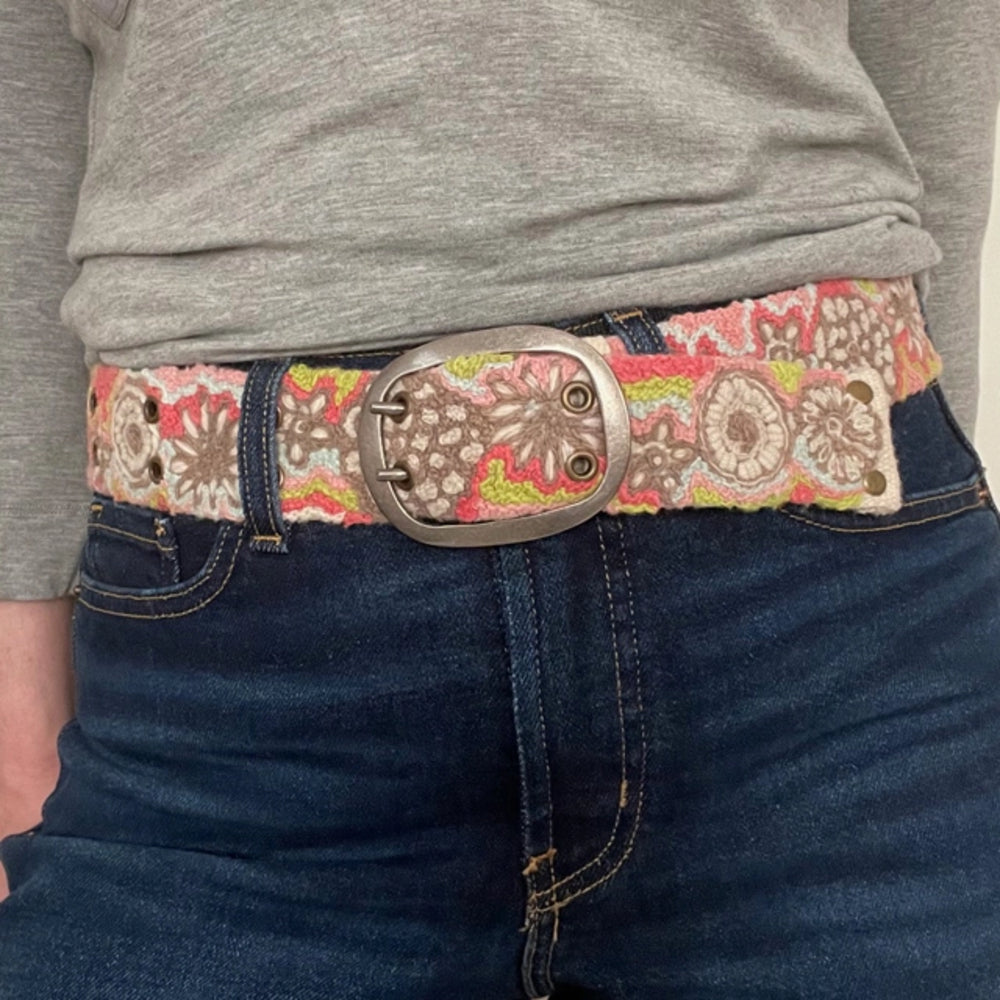 Person wearing a patterned belt with a large buckle on dark jeans.