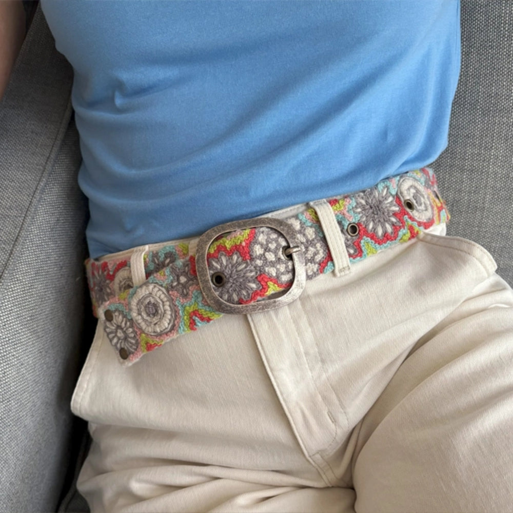 Person wearing a colorful belt with a floral pattern and large buckle.