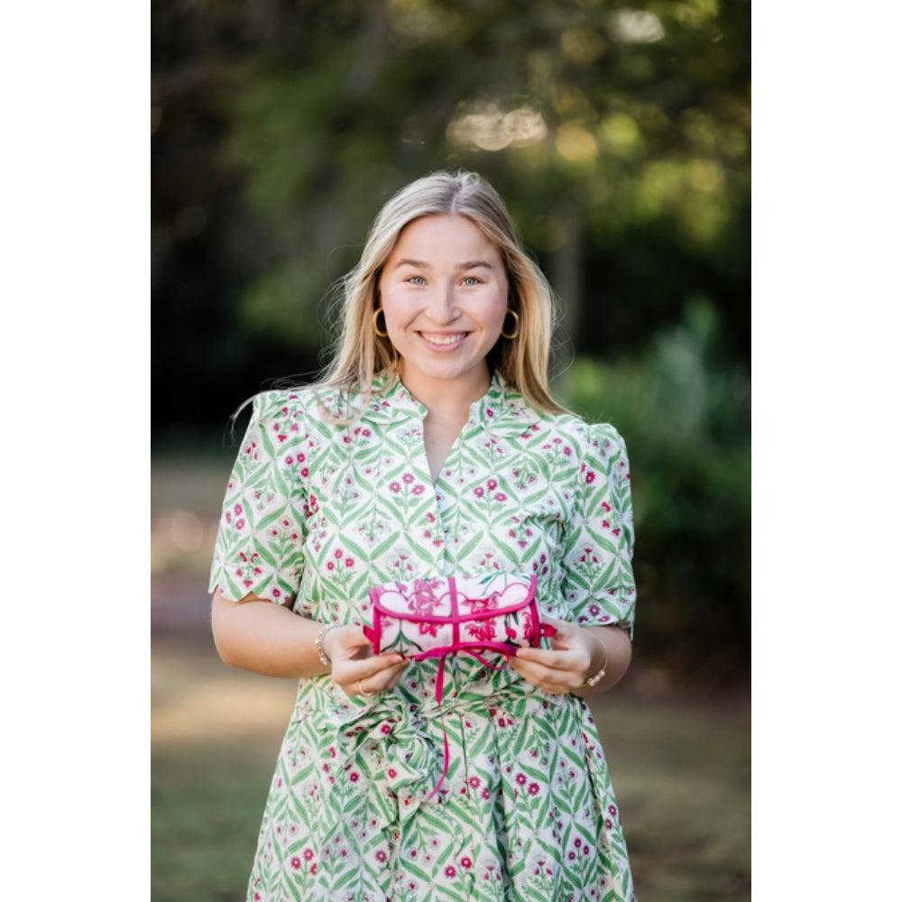 Woman in a green patterned dress holding a pink jewelry roll outdoors