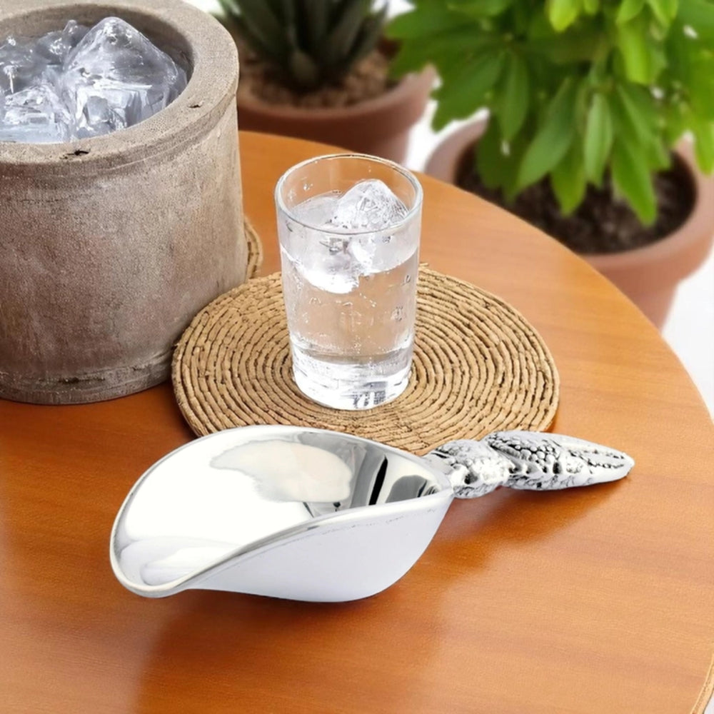 Silver ice scoop on a wooden table with a glass of water and ice cubes.