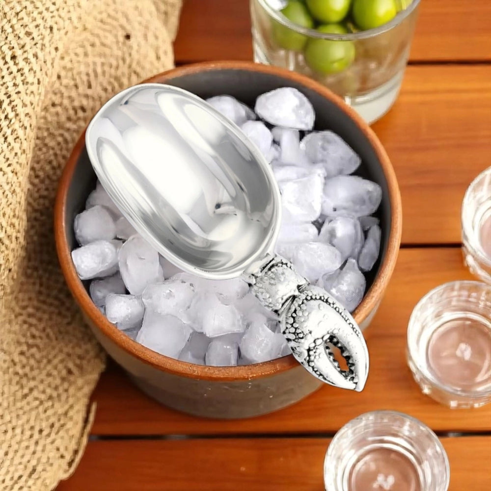 Silver ice scoop in a bowl of ice with glasses and grapes on a wooden surface