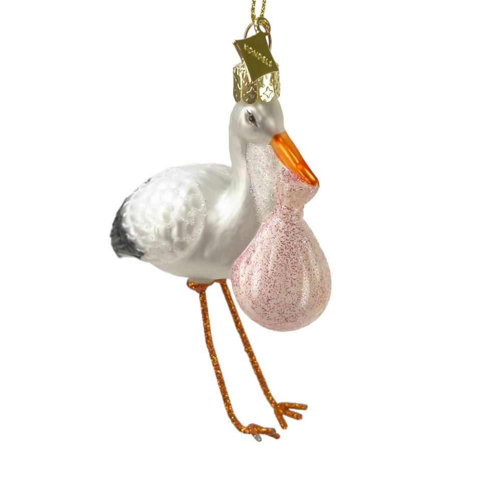 A white stork Christmas ornament carrying a pink glittery baby bag, with an orange beak and gold hanging loop, shown on a plain white background.