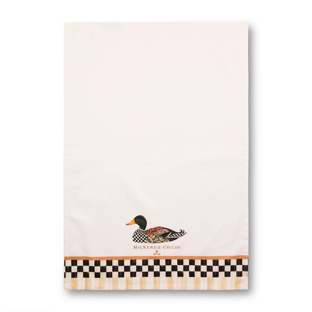 An off-white kitchen towel featuring a decorative mallard duck illustration near the bottom, with the text 'MCKENZIE CHILD' printed underneath. The towel is finished with a black and beige checkered border and a thin orange stripe above the duck.