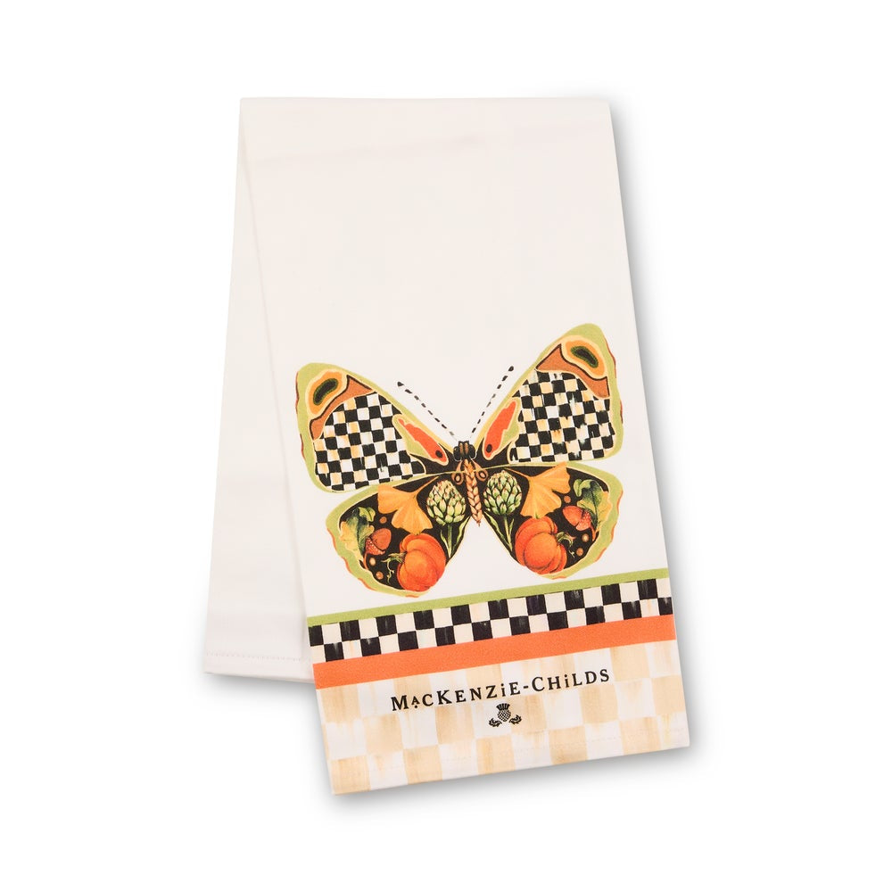 A white paper tea towel featuring a colorful butterfly design with checkered wings and fruit motifs, and the brand name 'MACKENZIE-CHILDS' printed near the bottom.