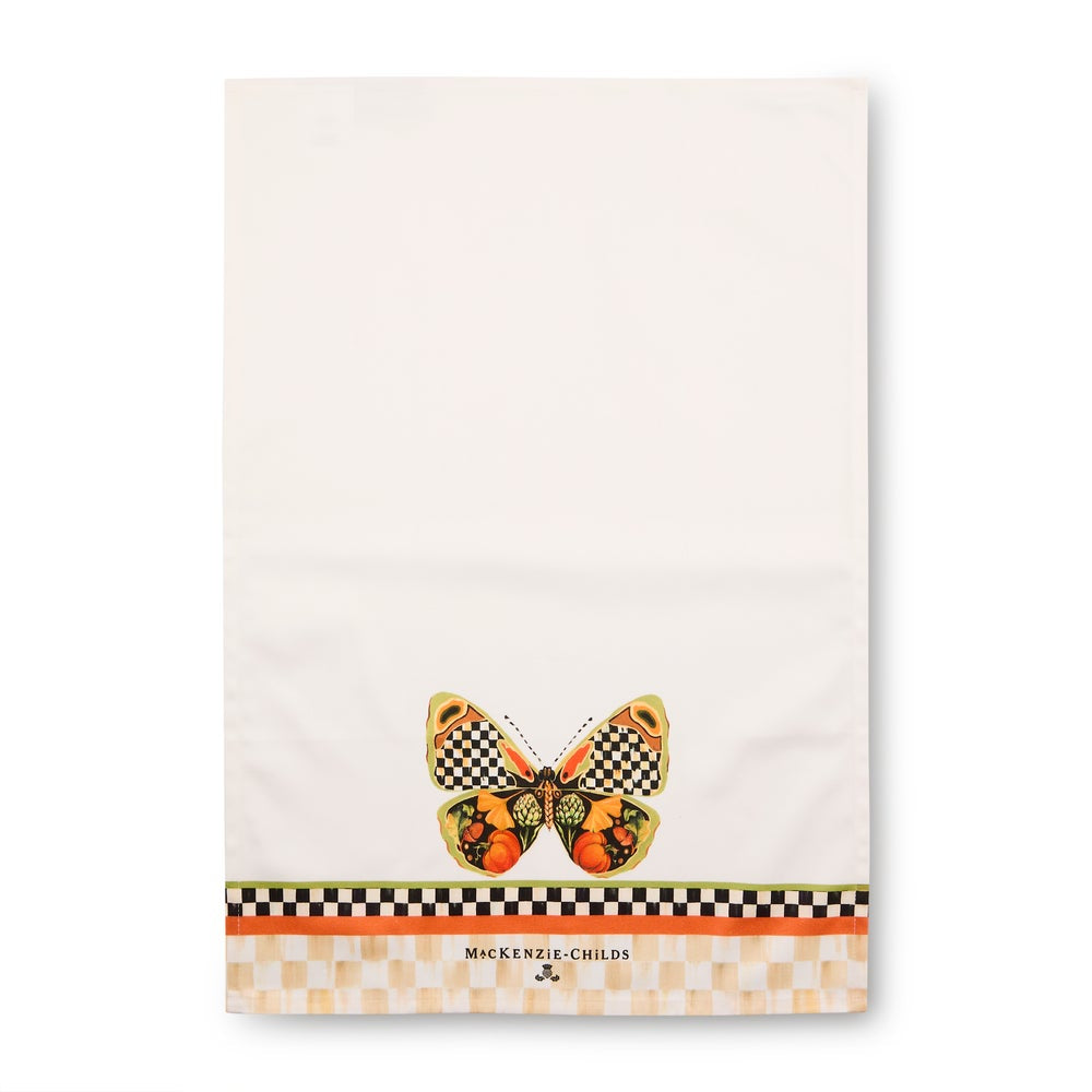An off-white kitchen towel featuring a decorative orange and black checkered butterfly near the bottom center, with a patterned border and the text 'MCKENZIE-CHILDS' printed on it.