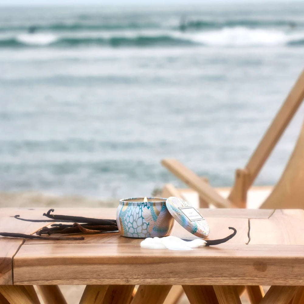 Candle with vanilla beans on a wooden table by the sea.