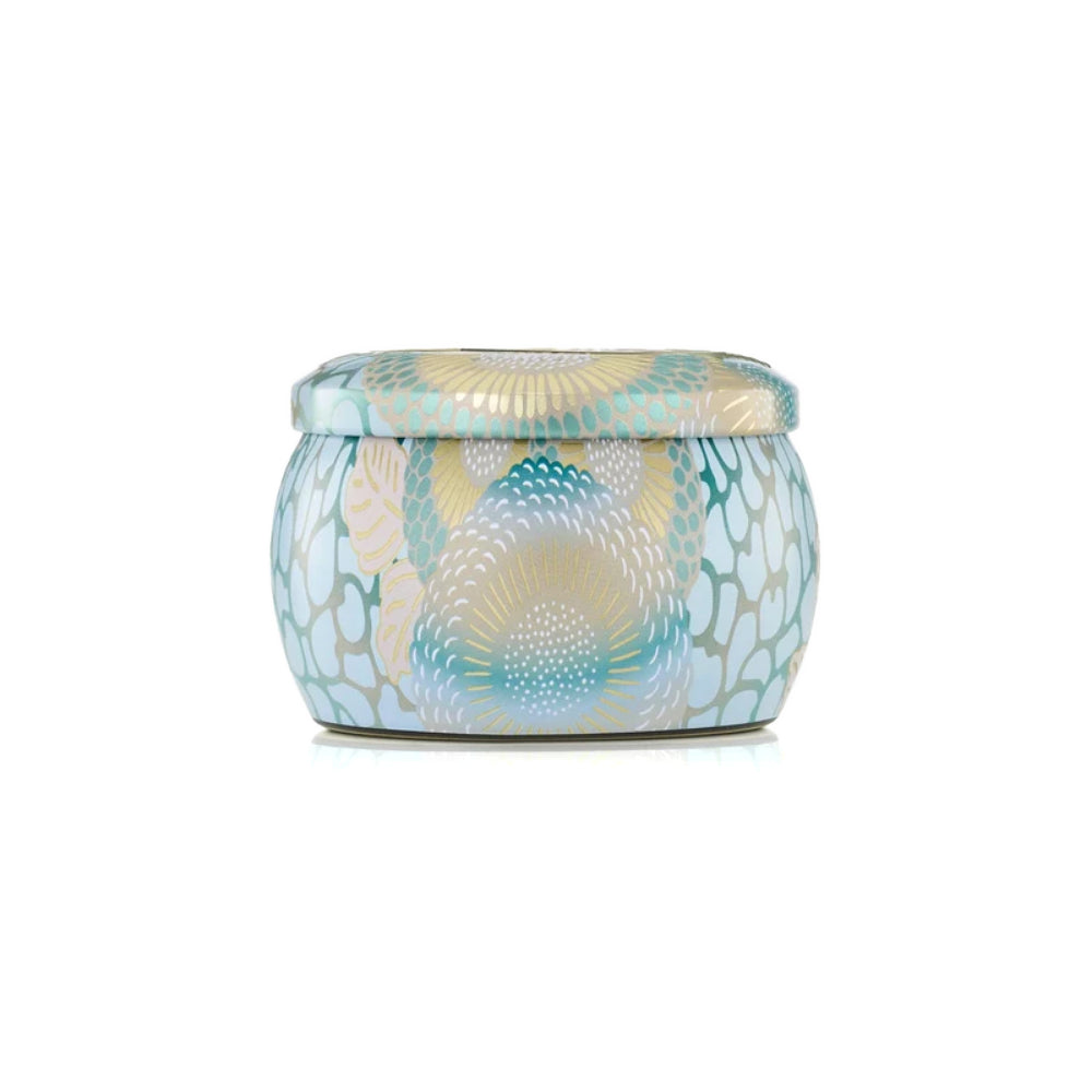 A small round lidded tin candle with a decorative abstract pattern in light blue, teal, beige, and white, centered on a plain white background.