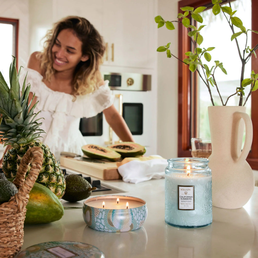 Woman in a kitchen with candles and fruit on the counter.