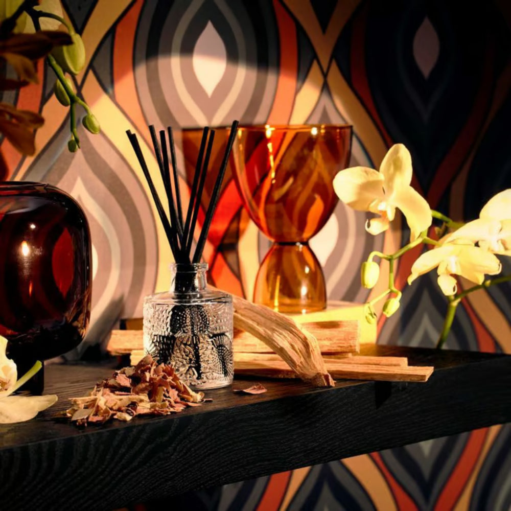 Baltic diffuser on a black shelf with flowers and other items against a colorful backround. 
