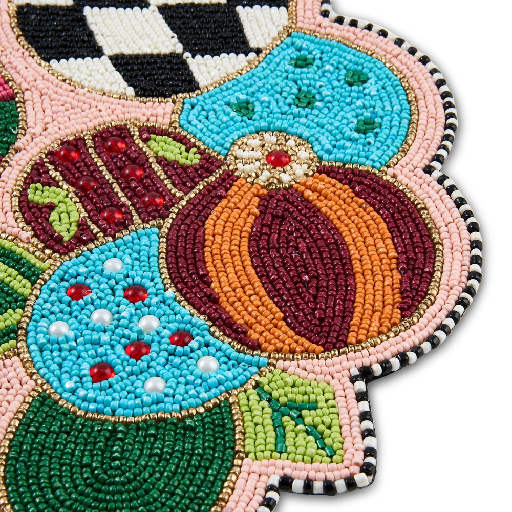 Close-up of a hand-beaded placemat or rug corner featuring stylized floral or fruit motifs in turquoise, burgundy, orange, green, pink, black, and white beadwork on a white background.