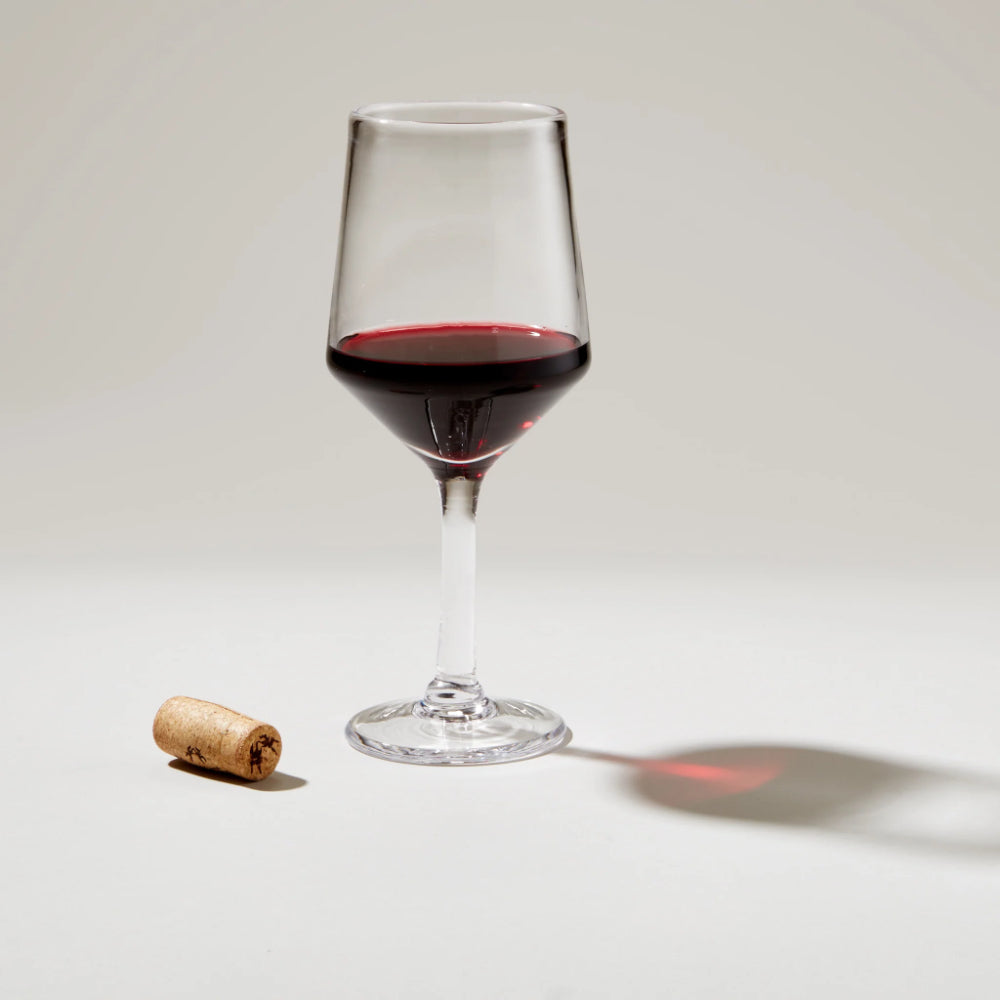 Wine glass with red wine and a cork on a light background