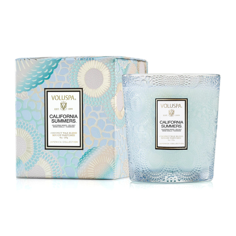 A Voluspa California Summers scented wax blend candle in a textured light blue glass vessel, shown next to its matching patterned packaging box on a white background.