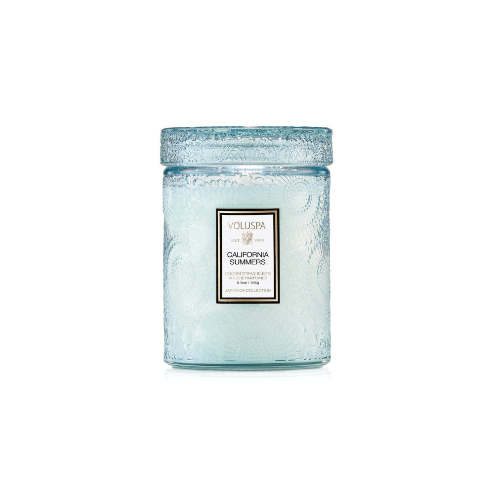 A Voluspa Candle in a textured light blue glass jar with a matching lid, featuring a white label with black text on a clean white background.