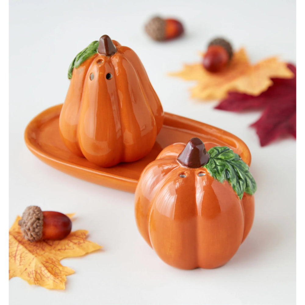 Pumpkin-shaped salt and pepper shakers on a white surface with fall leaves and acorns.