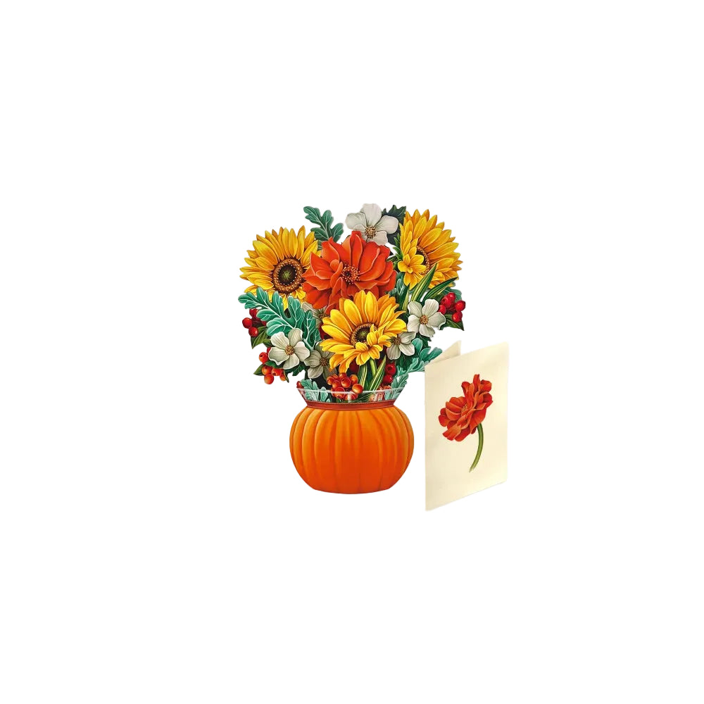 A floral arrangement featuring yellow sunflowers, orange and red flowers, green leaves, and small red berries in a pumpkin-shaped vase, with a small cream card showing a red flower beside it, set against a light gray background.