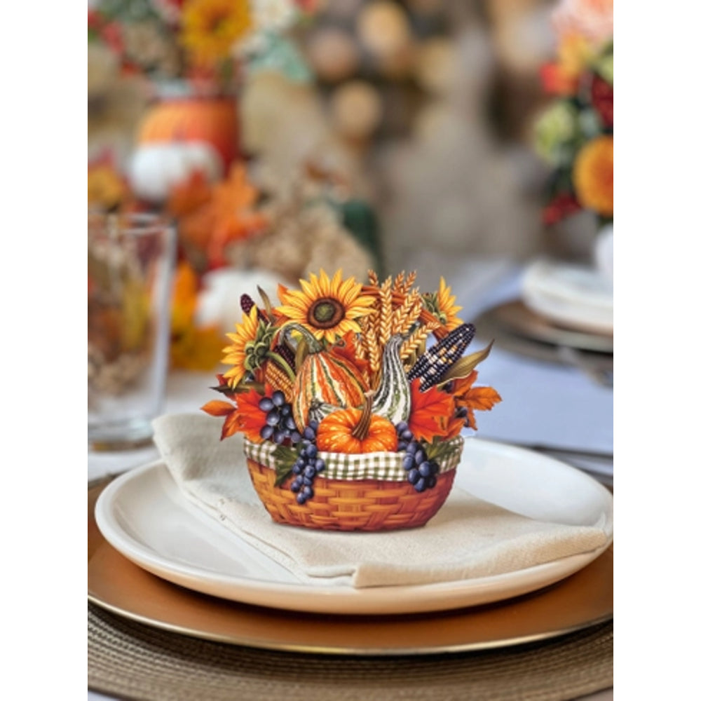 An autumn-themed tabletop centerpiece in a small woven basket, filled with sunflowers, pumpkins, gourds, wheat, blueberries, and a butterfly decoration, styled on a white plate with a folded cream napkin.