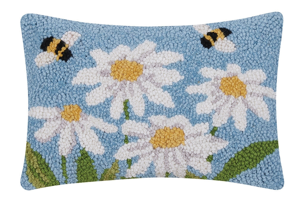 A rectangular accent pillow with a wool design depicting daisies and bees on a blue background.