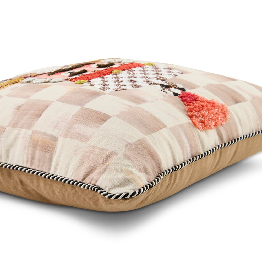 A square decorative throw pillow with a beige and cream checkered pattern, featuring a colorful embroidered design on top, a textured coral-pink tuft, and a black and beige striped piped edge.