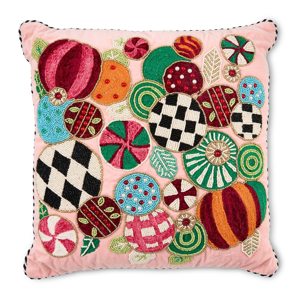 A square pink throw pillow featuring a colorful, festive embroidered pattern of candy canes, pumpkins, and geometric motifs, finished with black cord piping along the edges.