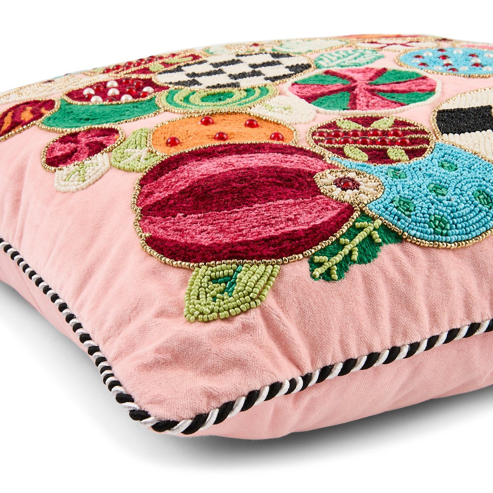 A square pink throw pillow featuring colorful, hand-embroidered and beaded botanical motifs, finished with a black and white striped piped edge.