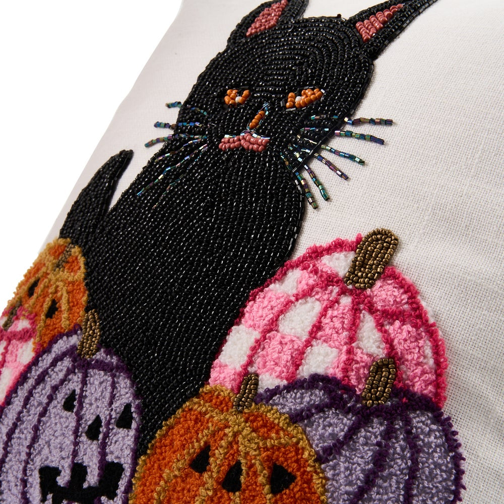 Close-up of a decorative textile featuring a black cat made of black beads, surrounded by colorful embroidered pumpkins in orange, pink, and purple on a white fabric background.