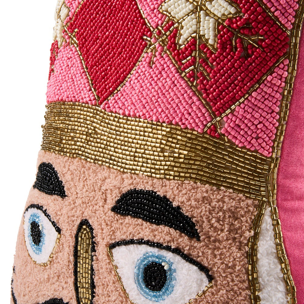 Close-up of a decorative nutcracker-themed textile or pillow featuring embroidered and beaded details in pink, red, gold, beige, black, white, and blue on a white background.