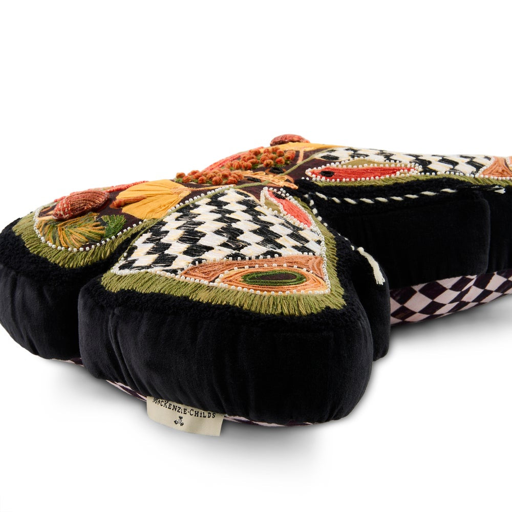 The side of a decorative butterfly-shaped cushion or pillow with embroidered details, featuring a black and white checkerboard pattern on the upper wings, orange and red accents, and embroidered autumn motifs including pumpkins and leaves on a black background.