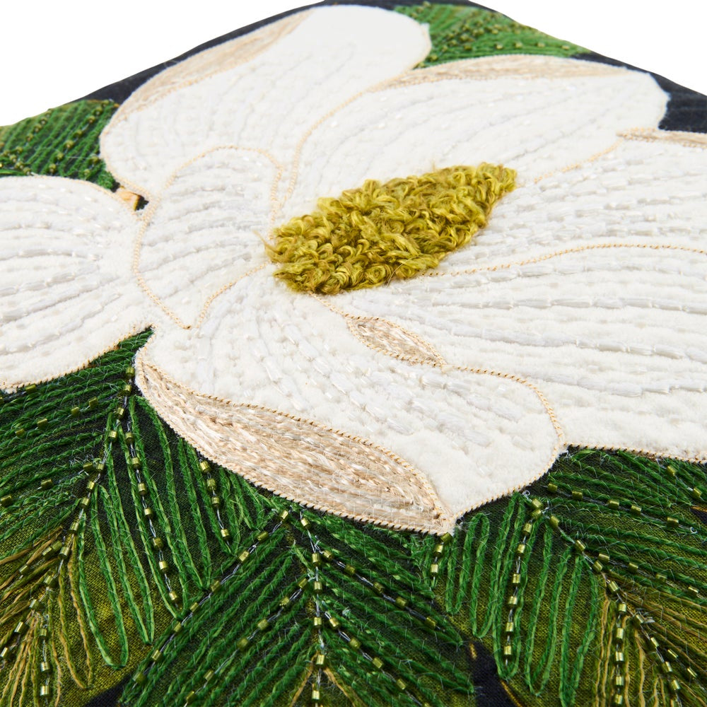 Close-up of a decorative embroidered cushion or textile featuring a large white flower with a textured olive-green center and green leafy stems on a dark background.