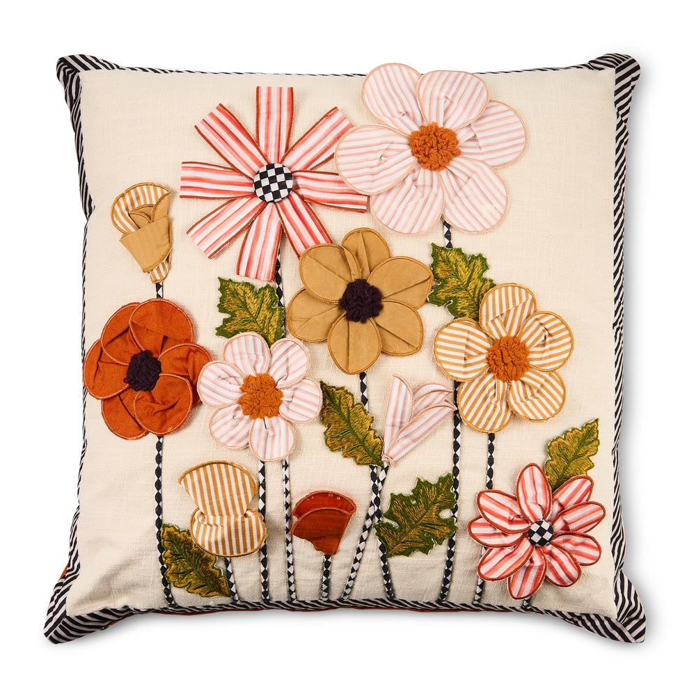 A square decorative throw pillow with a cream fabric base, featuring a colorful embroidered floral pattern with striped and textured flowers in orange, pink, beige, and green, finished with a black and white striped piped edge.